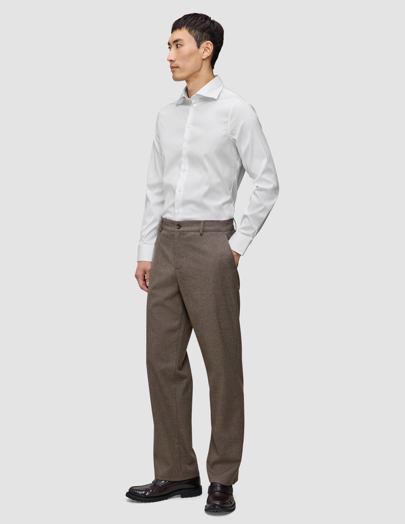 En mand iført en hvid Elevated Shirt White Slim og brune bukser står med den ene hånd i lommen.
